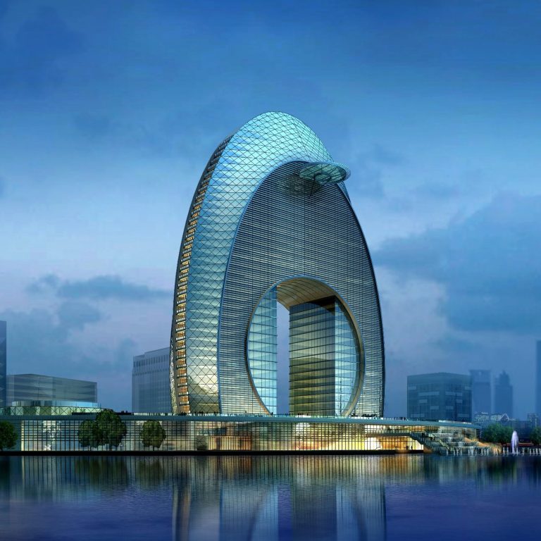 Futuristic skyscraper resembling a large oval shape beside a calm water body.